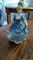 Front angle view of Royal Doulton Elizabeth figurine in blue dress posed on wooden table.