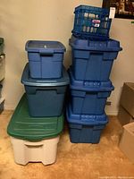Stack of six plastic totes in blue, green, and white colors with lids and one blue milk crate on top.
