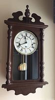 Front view of the wooden pendulum wall clock showing the clock face and carved wooden frame.