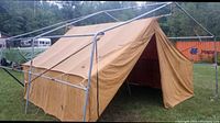 A tan canvas prospector tent stretched on a metal frame, the frame is not included in the lot, the canvas tent is shown in outdoor setting.