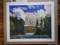 Framed print showing autumn landscape with black spruce trees, colorful sky with brushstroke texture.