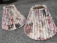 Pair of floral pleated lampshades placed on asphalt ground, showing a sideways angle to highlight the overall shape and fabric pattern.