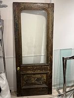 Front view of the antique door showing chipped dark brown and beige paint, large rectangular glass panel, raised panel base, brass door knob.