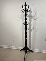 Full view of black wooden coat rack showing overall height and base with multiple hooks