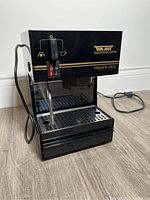 Front angle showing black Waring espresso machine with steam wand, power switch, drip tray, and power cord visible.