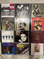 Top view of 12 CD cases arranged in four rows showing album artwork from classic rock and pop artists.