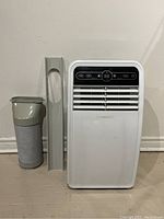 Frontal view of white portable air conditioner with vent hose and window bracket on the side.