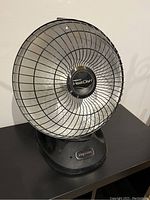 Front view of the Presto Heat Dish portable heater on a table showing the parabolic metal wire cage and base.