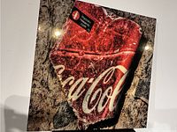 Front view of square resin art on wood featuring a realistic broken Coca Cola logo on a textured, cracked background.