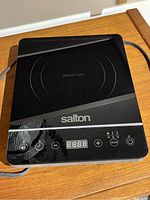 Front view of Salton induction cooktop on wood surface, showing control panel and cooking surface