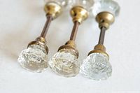 Three vintage glass handle door knobs with brass mounting hardware lying flat, visible from an angled close-up view showing glass designs and rods.