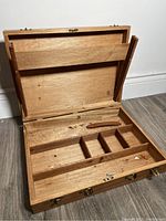Open painter's box showing wooden interior with multiple compartments and internal dividers for art supplies storage.