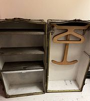 Open steamer trunk showing inside with barnboard shelves on left and wooden clothing hanger on right side.