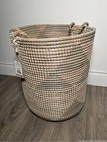Full outside view of tall round woven wicker laundry basket with rope handles.