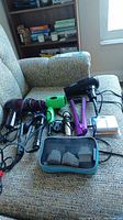 Photo of hair dryers, curling and flattening irons with power cords and travel adapters pouch on fabric chair
