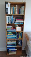 Photo of wooden bookshelf filled with various books across shelves, showing mixed collection.