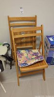 Two wooden folding chairs, one with a colorful floral cushioned seat, standing against wall near boxes and a small table.