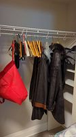 Photo of jackets hanging on wire closet rack with assorted hangers and a red garment bag visible on left.