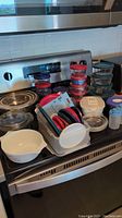 Overview of various food storage and cookware items including glass Pyrex containers with lids, plastic containers, and lids on stovetop