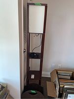 Full view of tall wood frame floor lamp with multiple shelves and a white rectangular lamp shade, cord visible inside shelf