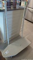 Small folding table top ironing board and white folding drying rack leaning against a kitchen counter, showing the grid pattern cover and rack structure.