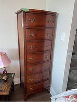 Three-quarter front view of tall narrow cabinet showing seven drawers and brass hardware