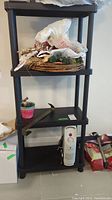 Photo of the narrow black resin shelf with four levels and decorative items stacked on top. Small white Airworks electric radiator style heater placed on bottom shelf.