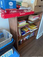 Front view of wood bookcase filled with books and boxed board games on top.