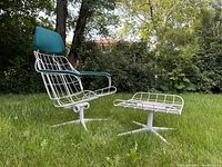 Side angled view of Homecrest steel wire swivel recliner chair with matching ottoman on grass outdoors. Chair has teal upholstered headrest and armrest cushions, missing seat cushion. Ottoman has steel wire construction, missing cushion.