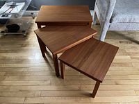 Three tables partially nested on wood floor with sofa in background