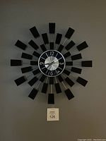 Front view of the black and metallic starburst wall clock mounted on a wall, showing overall design and clock face.