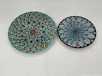Full view of two ceramic art plates by Deruth, one larger with teal/yellow flower pattern, one smaller with black background and pink/teal floral design.