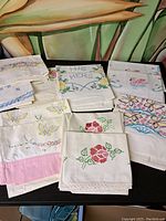 Several assorted vintage cloth napkins laid out on table showing embroidery designs including floral patterns, butterflies, swans, and 'His' and 'Hers' text
