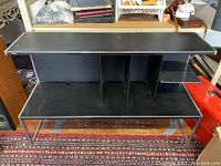 Front view of black lacquered wood cabinet with multiple compartments and lower shelf supported by metal legs