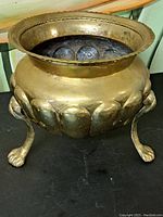 Front angle showing the brass pot with three ornate claw feet and decorative rounded embossing around the body.
