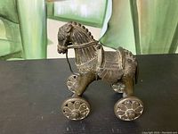 Side view of brass horse toy showing detailed patterns on body and wheels