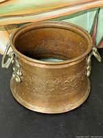 Full view of the bronze/brass bucket showing embossed floral decoration and shape.