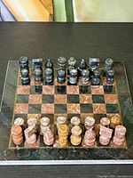 Full view of carved stone chess set laid out on a polished stone chessboard, showing all pieces arranged in starting position.