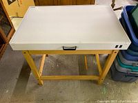 Full view of the drawing table/workstation desk with angled light gray surface and wooden base.