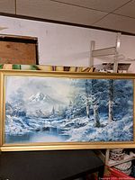 Full view of the framed winter landscape painting showing a snowy scene with mountain, trees, and pond in muted blue and white tones.