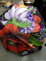 Umbrella opened, showing the large floral print with red poppies, white and purple flowers, and green leaves on a black background