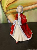 Front view of the figurine showing the lady in a red cloak holding the collar, face and gown visible.