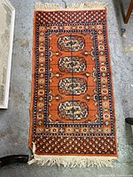 Full view of the vintage orange rug with central medallions and fringed ends.