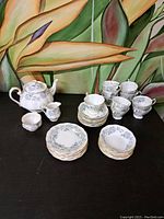 Full view of tea set arranged on black surface against floral backdrop