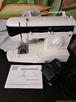 Full view of SINGER 2732 electric sewing machine with instruction manual and foot pedal in front.