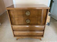 Front view of the vintage mid-century dresser showing four drawers and brass decorative pulls on top drawers.