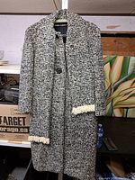Front view of black and white tweed coat with button closure and cream fringe detail