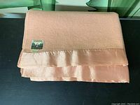 Folded peach wool blanket showing satin trim and Modertia label.
