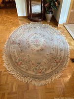 Oval floral carpet rug laid on parquet floor, showing full length and oval shape with fringed edges and floral pattern.
