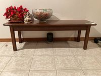 Rectangular wood coffee table placed against wall on tiled floor. Top surface has scratches. Decorative items on top which are not included.